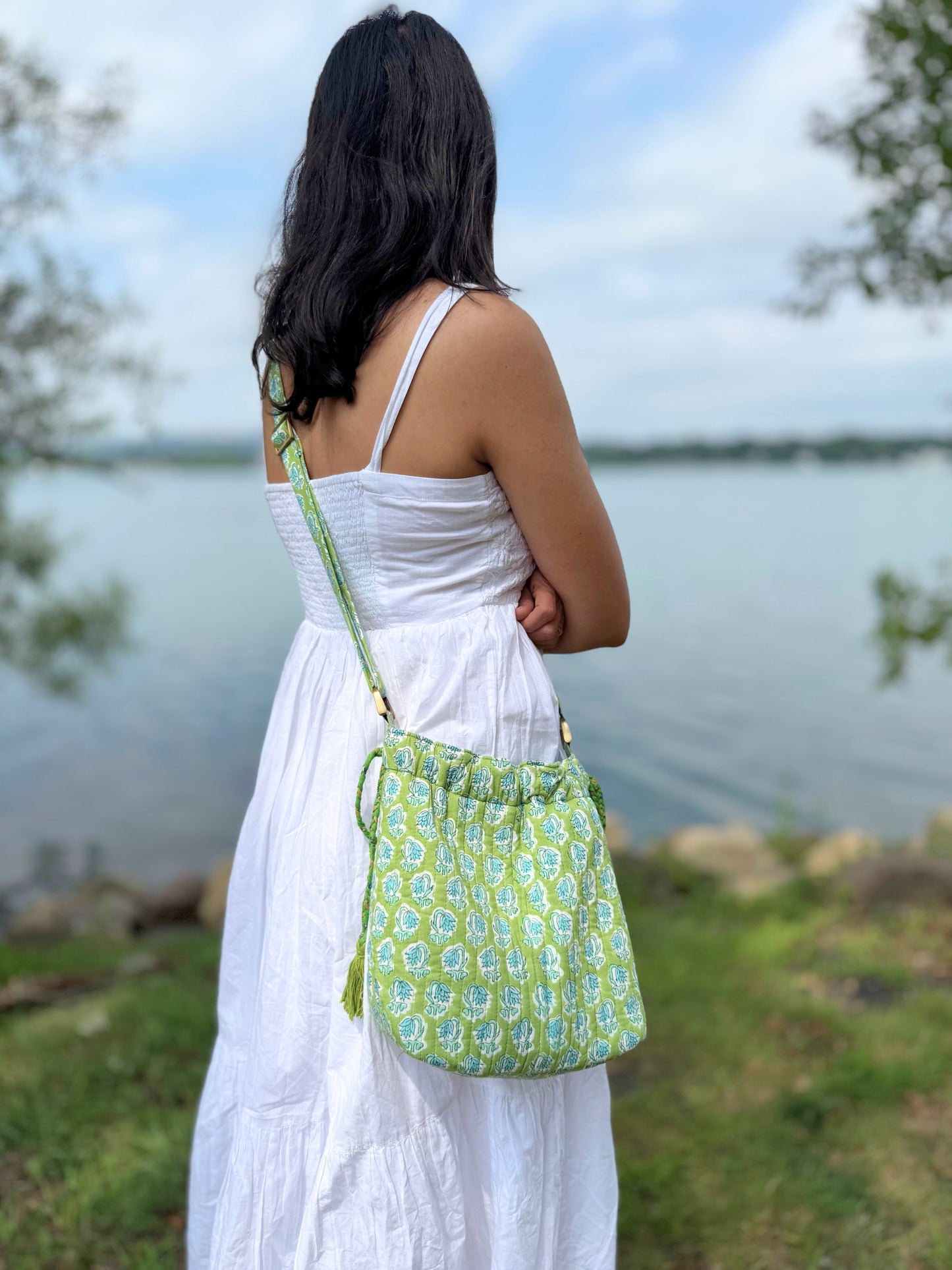 House of Mulmul - Garden Wayfarer Bucket Bag, Cotton bag, Crossbody sling bag. Woman in a white dress with a green floral bag standing by a lake.