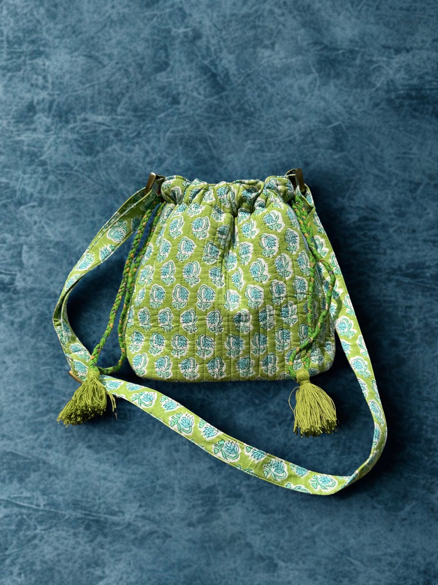 House of Mulmul - Garden Wayfarer Bucket Bag, Cotton bag, Crossbody sling bag. Green patterned drawstring bag with tassels on a gray background