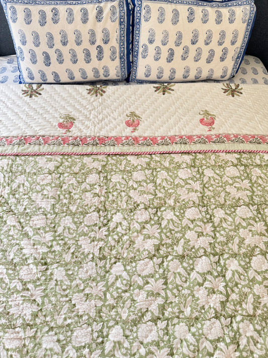 House of Mulmul - Blockprint Cotton Quilt Reversible. A green and white floral quilted bedspread with a pink and white border, styled on a bed with two matching blue and white patterned pillows.