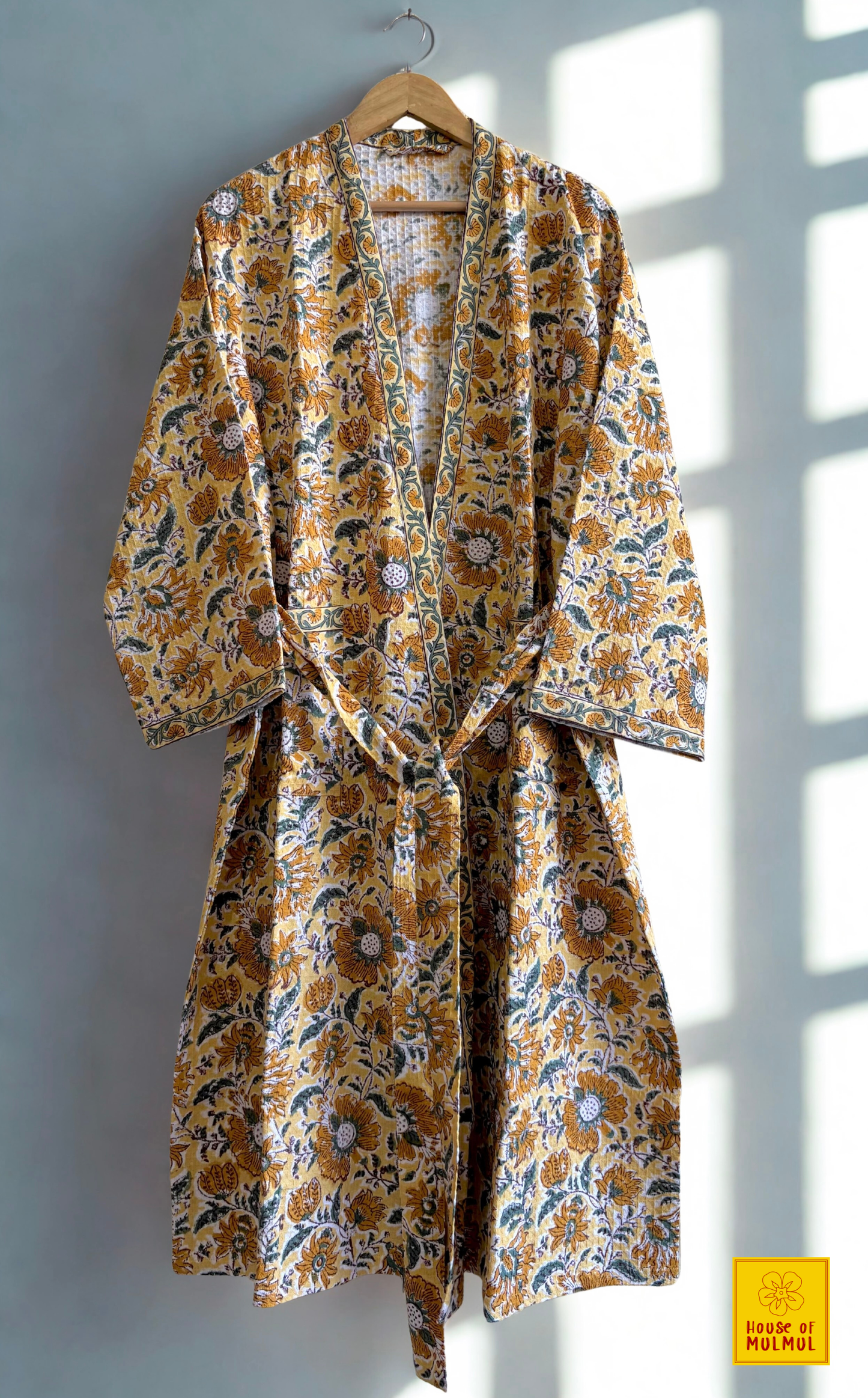 House of Mulmul - Blockprinted Cotton Bathrobe. Yellow floral patterned robe hanging on a wooden hanger against a light background