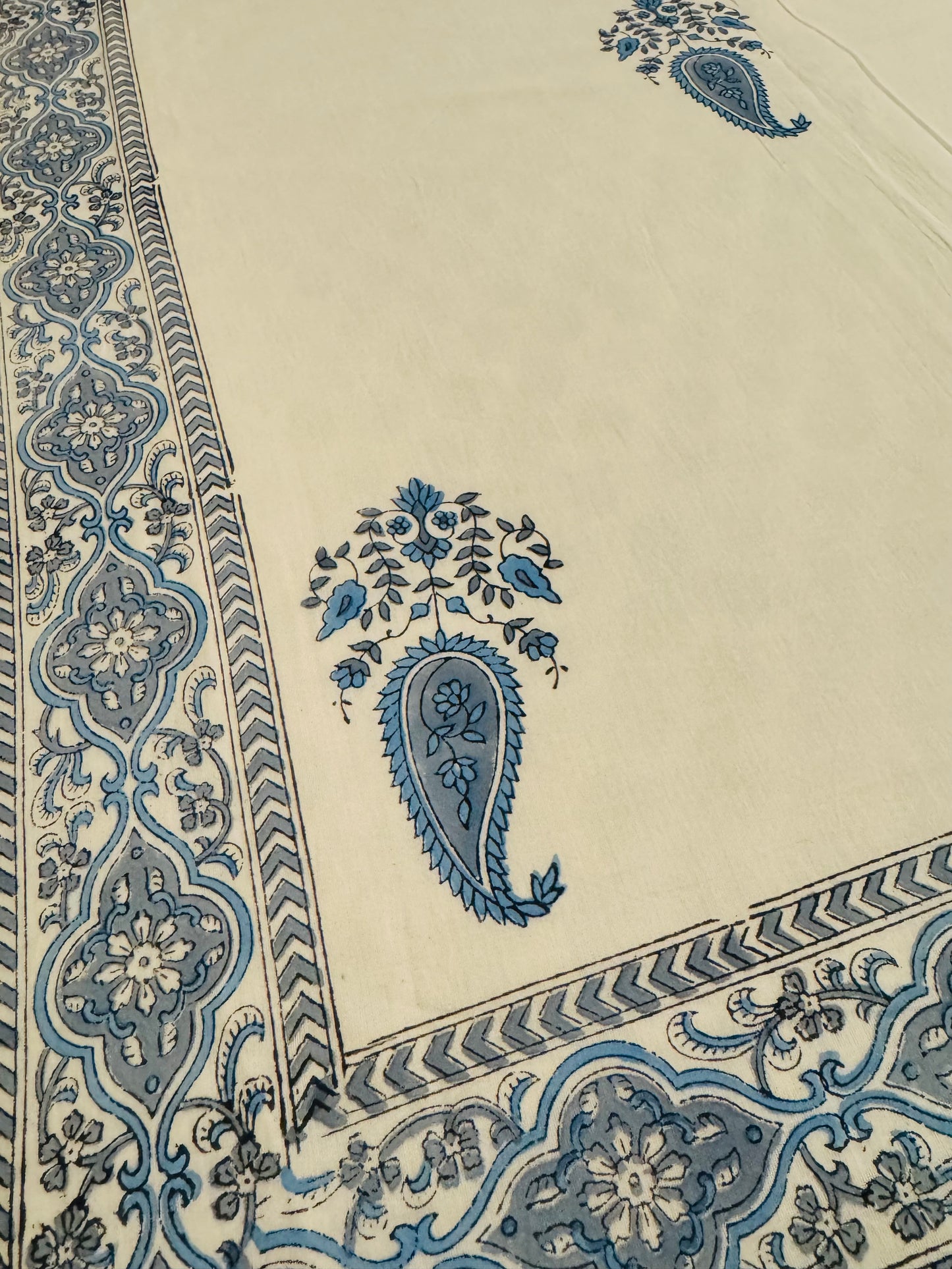 House of Mulmul - Coverlet Dohar blanket. Bedroom with reversible cotton coverlet blanket. Muslin dohar with boota paisley leaf and blue and grey colors, white background. Bedroom with floral curtains, mirror.