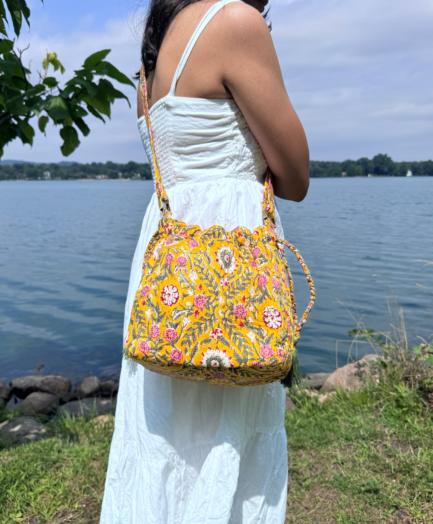 House of Mulmul - Garden Wayfarer Bucket Bag, Cotton bag, Crossbody sling bag. Woman in a white dress holding a yellow floral handbag by a lake