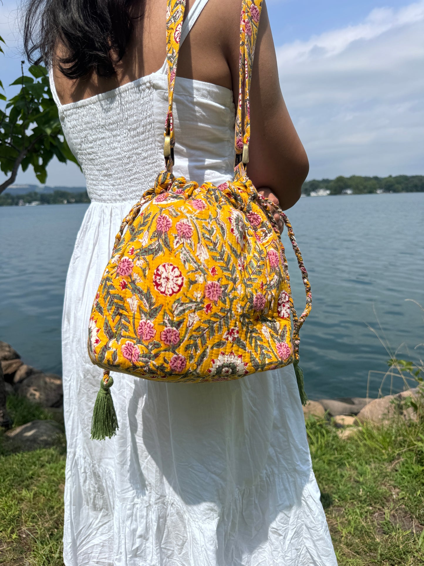 House of Mulmul - Garden Wayfarer Bucket Bag, Cotton bag, Crossbody sling bag. Person holding a yellow floral bag outdoors with a white tarp and blue sky in the background
