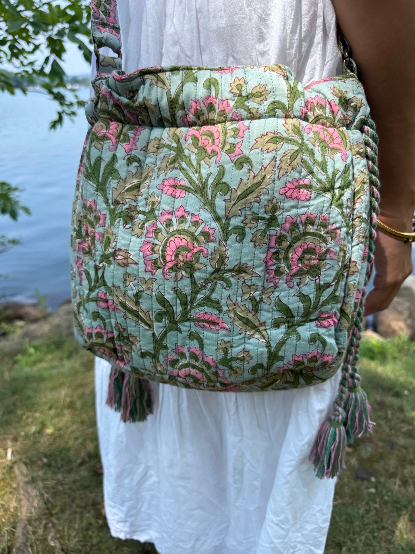 House of Mulmul - Garden Wayfarer Bucket Bag, Cotton bag, Crossbody sling bag. Person holding a floral-patterned bag by a body of water with a decorative border.