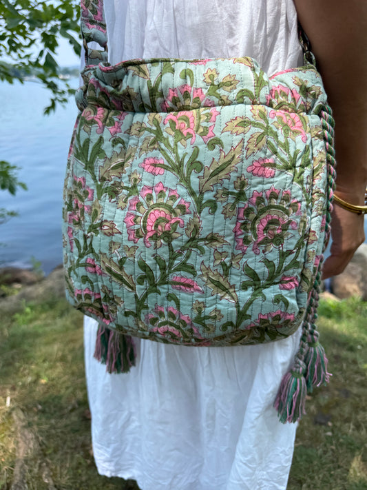 House of Mulmul - Garden Wayfarer Bucket Bag, Cotton bag, Crossbody sling bag. Person holding a floral-patterned bag by a body of water with a decorative border.