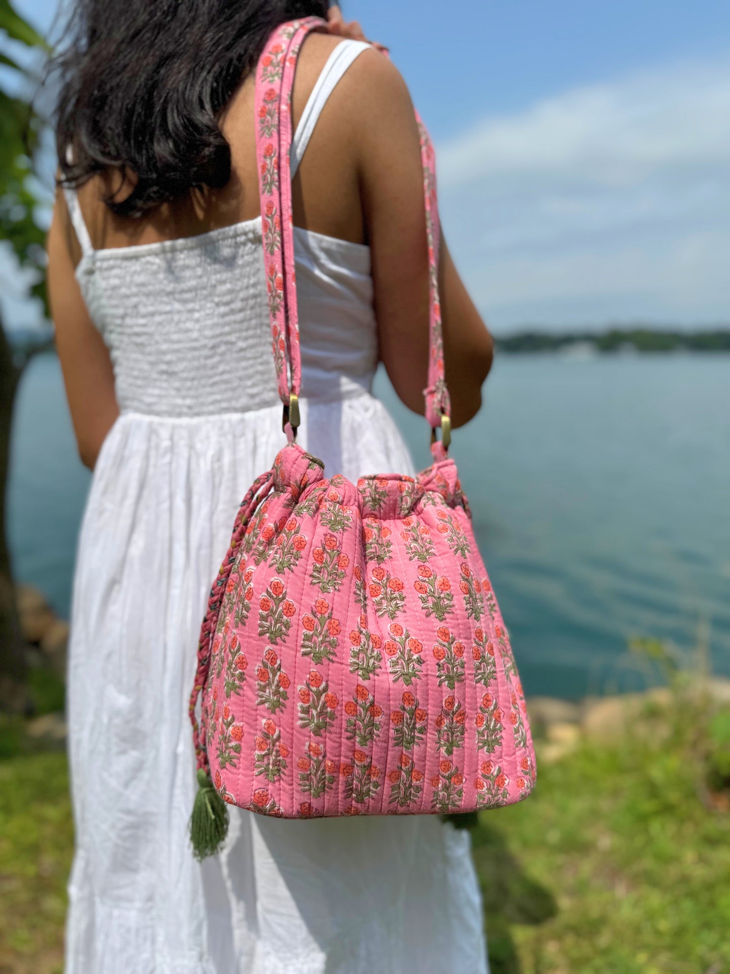 House of Mulmul - Garden Wayfarer Bucket Bag, Cotton bag, Crossbody sling bag. Woman holding a pink floral handbag by a body of water