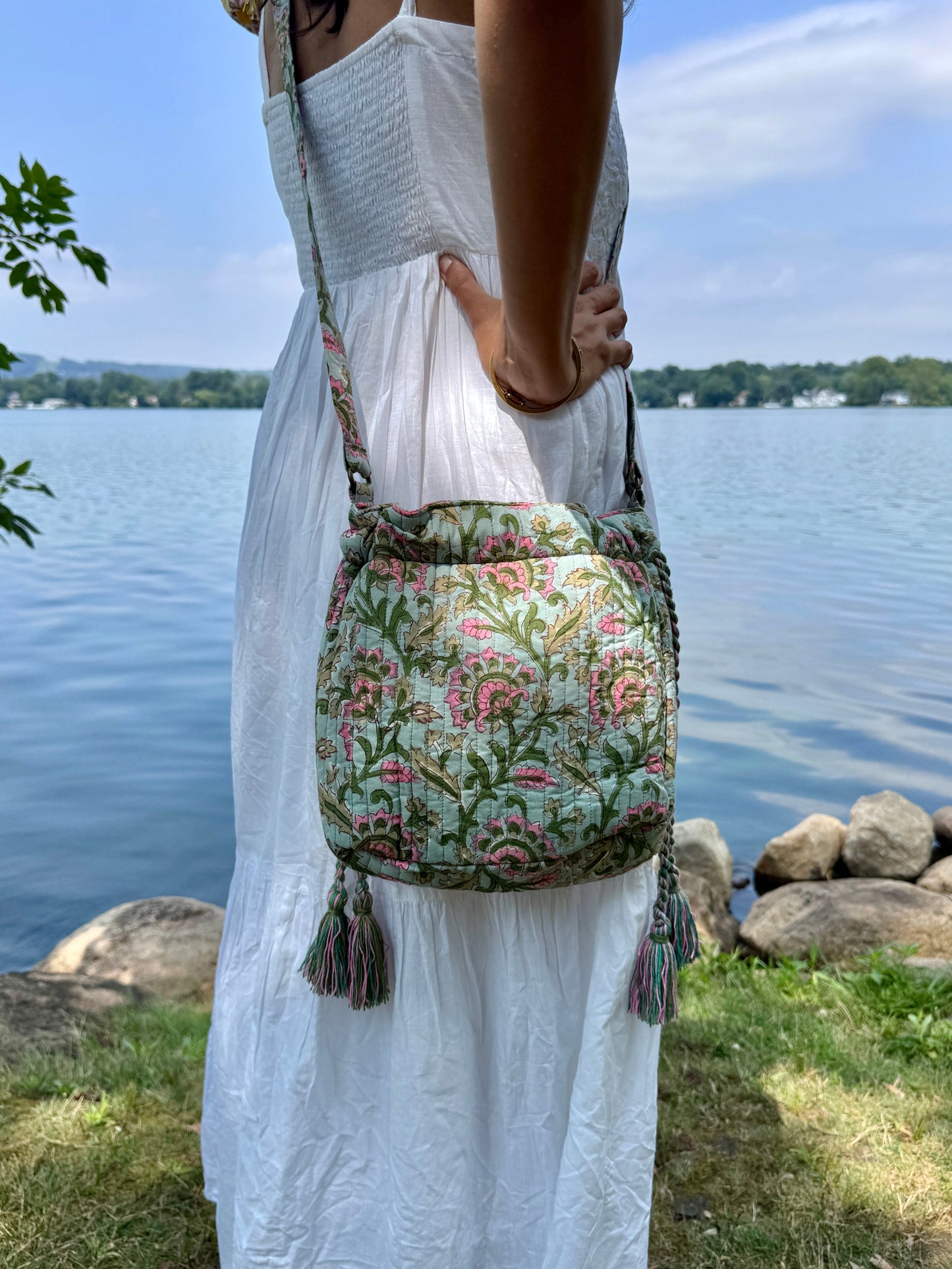 House of Mulmul - Garden Wayfarer Bucket Bag, Cotton bag, Crossbody sling bag. Person holding a floral-patterned bag by a body of water with a decorative border.
