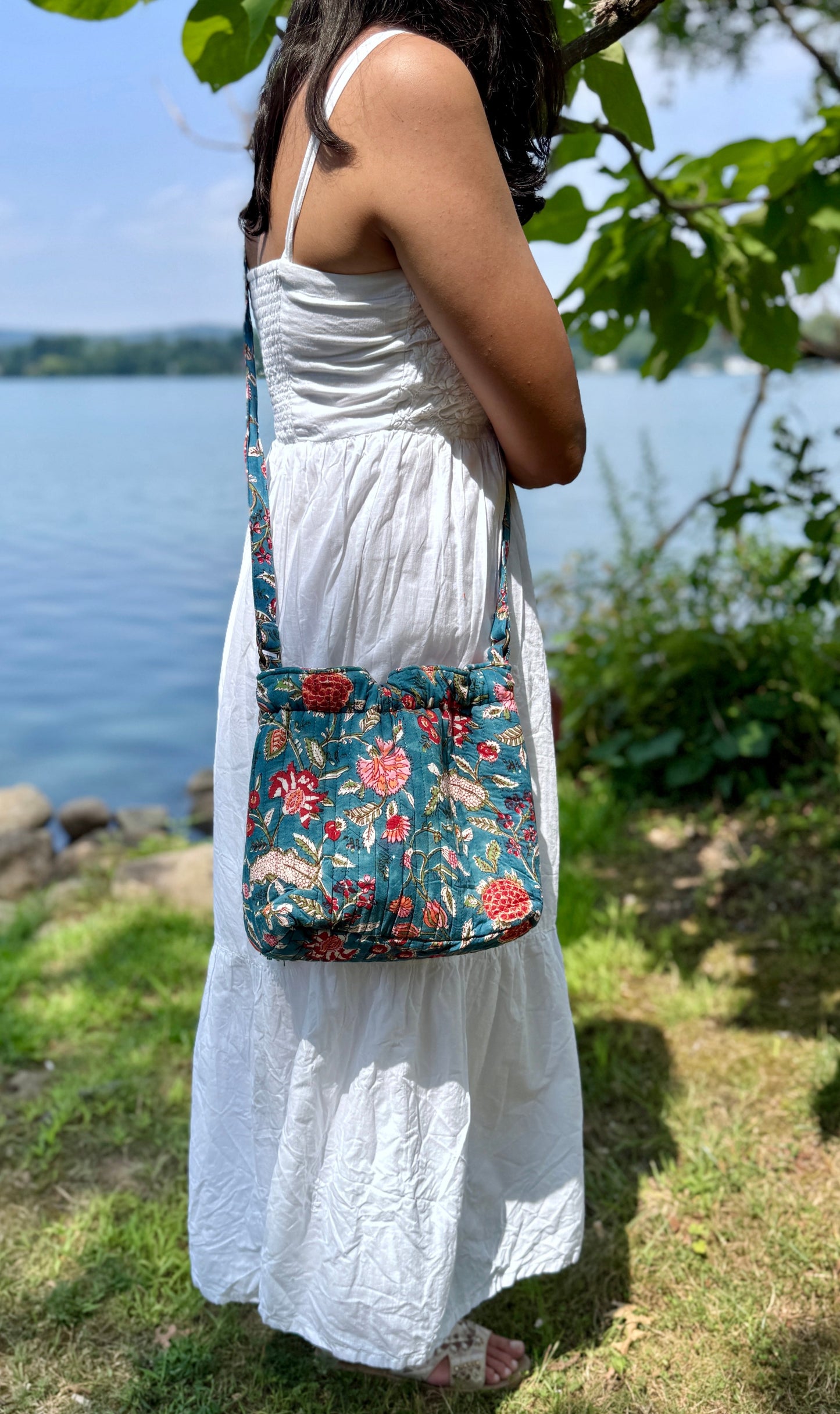 House of Mulmul - Garden Wayfarer Bucket Bag, Cotton bag, Crossbody sling bag. Woman in a white dress holding a floral-patterned bag by a body of water.