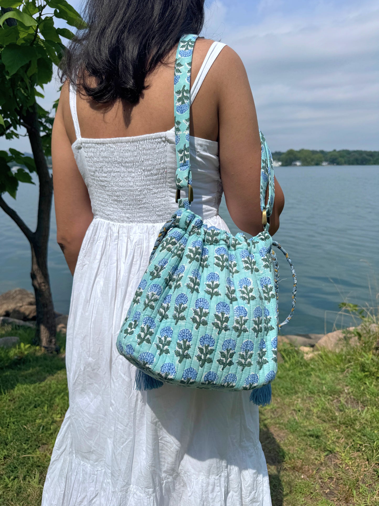 House of Mulmul - Garden Wayfarer Bucket Bag, Cotton bag, Crossbody sling bag. Person holding a blue floral-patterned bag by a body of water