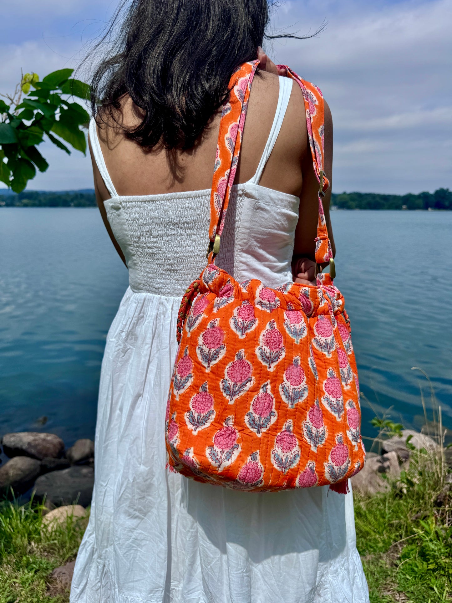 House of Mulmul - Garden Wayfarer Bucket Bag, Cotton bag, Crossbody sling bag. Woman holding an orange patterned bag by a lake