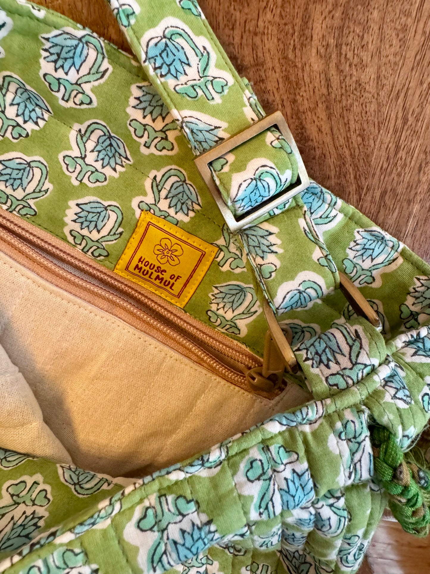 House of Mulmul - Garden Wayfarer Bucket Bag, Cotton bag, Crossbody sling bag. Green patterned bag with the brand label and adjustable hook on a wooden surface.