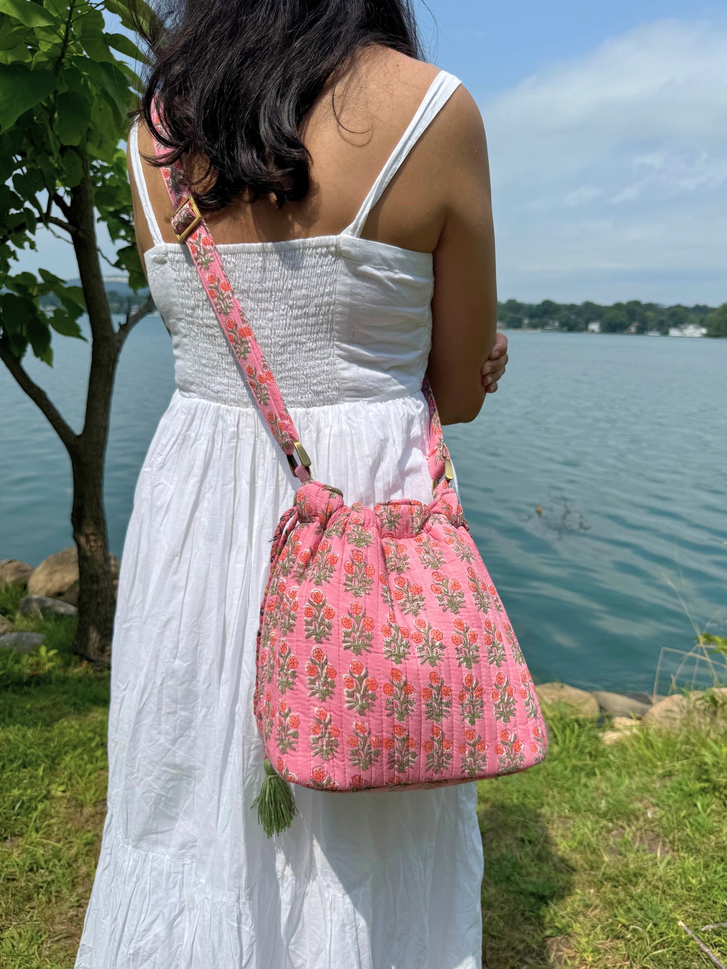 House of Mulmul - Garden Wayfarer Bucket Bag, Cotton bag, Crossbody sling bag. Woman in a white dress holding a pink patterned bag by a lake