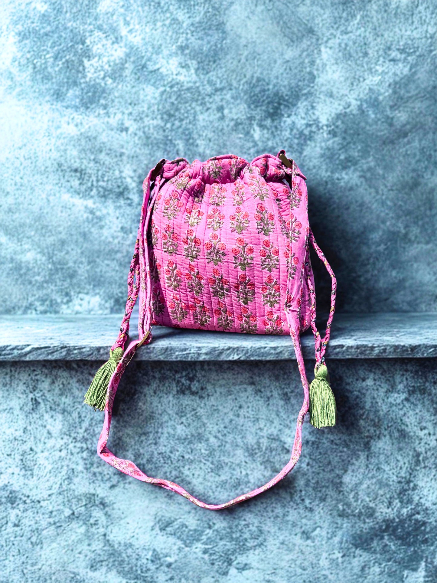 House of Mulmul - Garden Wayfarer Bucket Bag, Cotton bag, Crossbody sling bag. Pink embroidered drawstring bag with tassels on a stone ledge