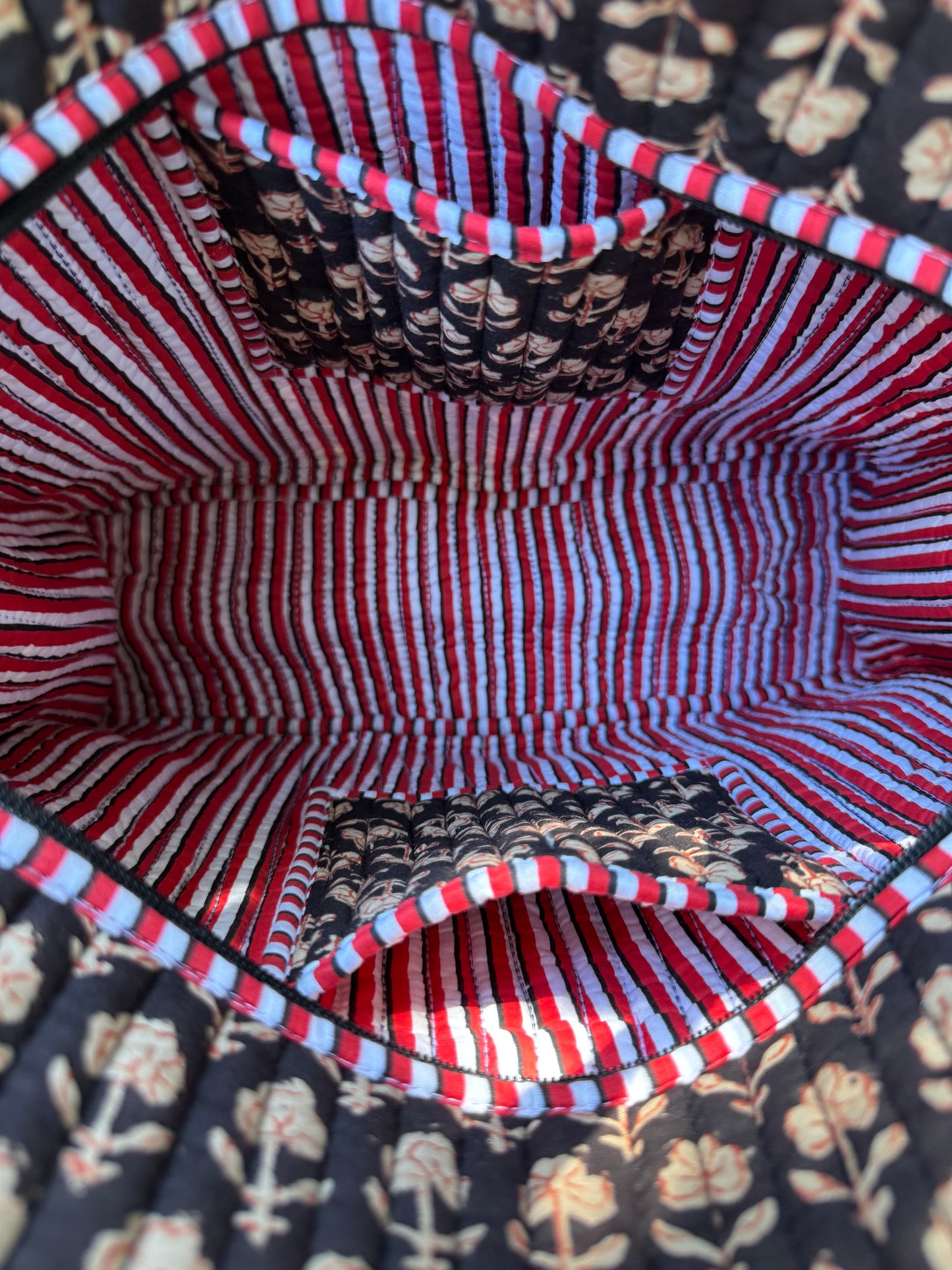 House of Mulmul - Cotton Tote Bag. Close-up of a fabric interior with red and white stripes and black pattern, on a floral background.