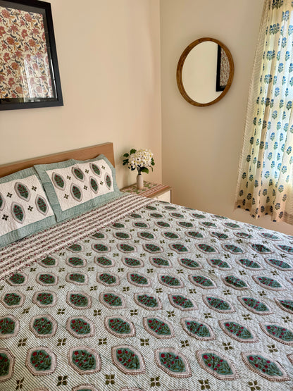 House of Mulmul - Blockprinted Cotton Bedcover. Reversible Bedspread. Bedroom with a floral-patterned quilt on a bed, framed mirror, and curtains.