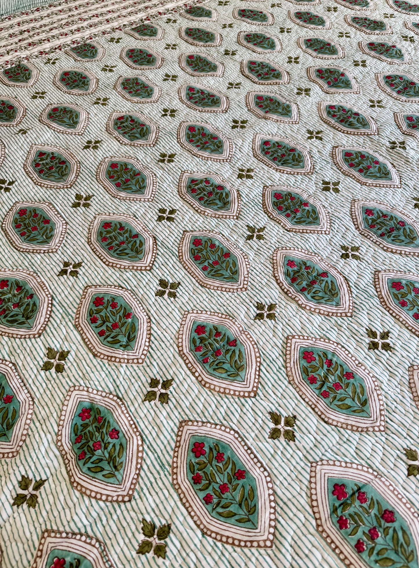 House of Mulmul - Blockprinted Cotton Bedcover. Reversible Bedspread. Close-up of a patterned fabric with geometric shapes and floral elements.