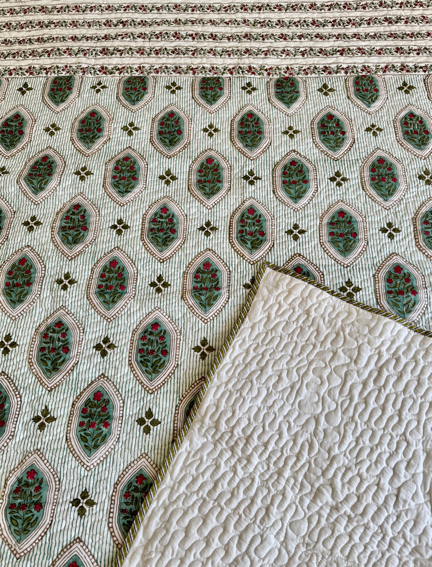 House of Mulmul - Blockprinted Cotton Bedcover. Reversible Bedspread. Bedroom with a floral-patterned quilt on a bed, framed mirror, and curtains.