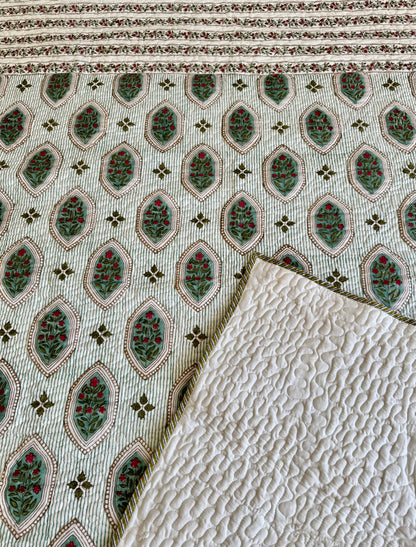 House of Mulmul - Blockprinted Cotton Bedcover. Reversible Bedspread. Bedroom with a floral-patterned quilt on a bed, framed mirror, and curtains.