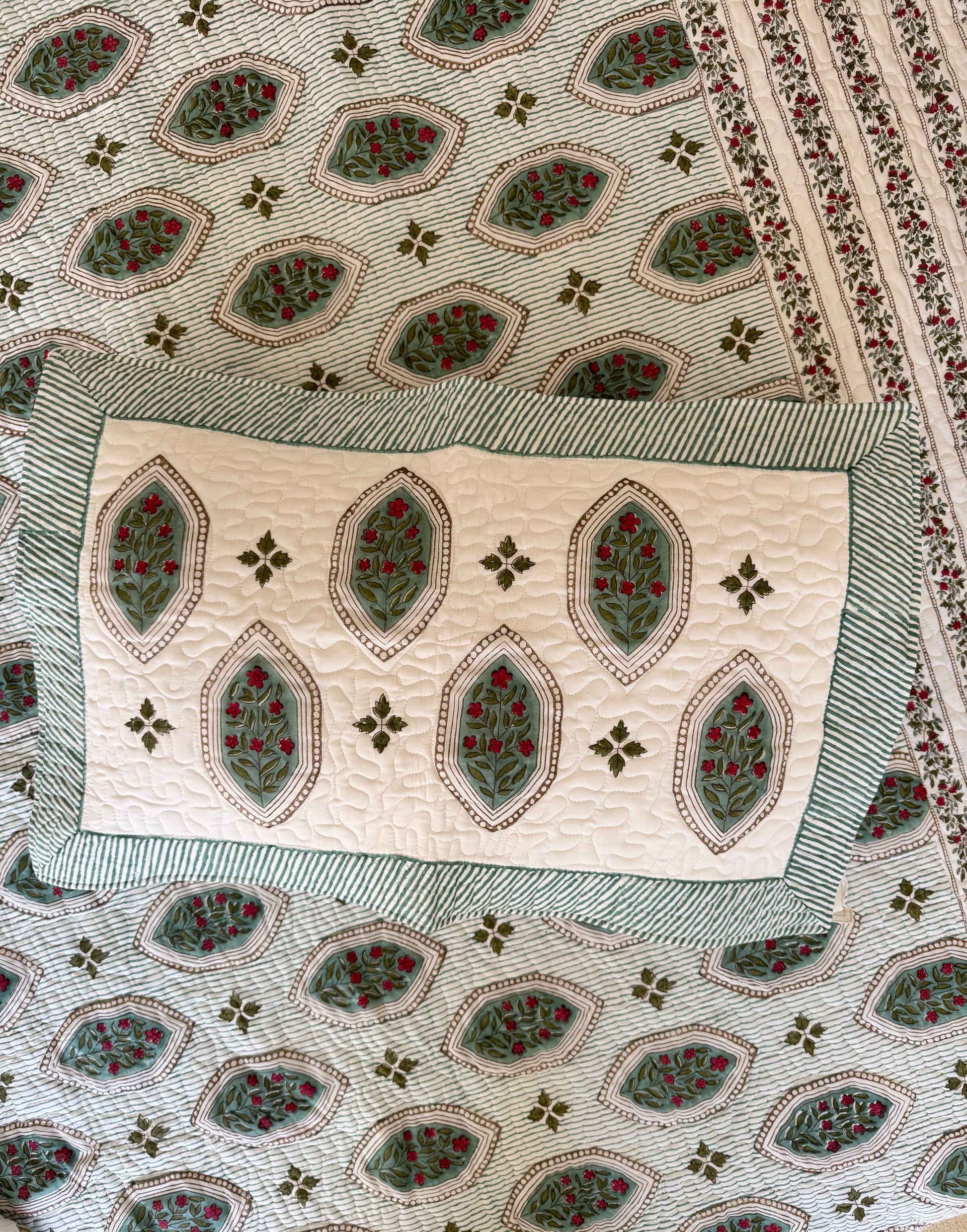 House of Mulmul - Blockprinted Cotton Bedcover. Reversible Bedspread. Bedroom with a floral-patterned quilt on a bed, framed mirror, pillowcases and curtains.