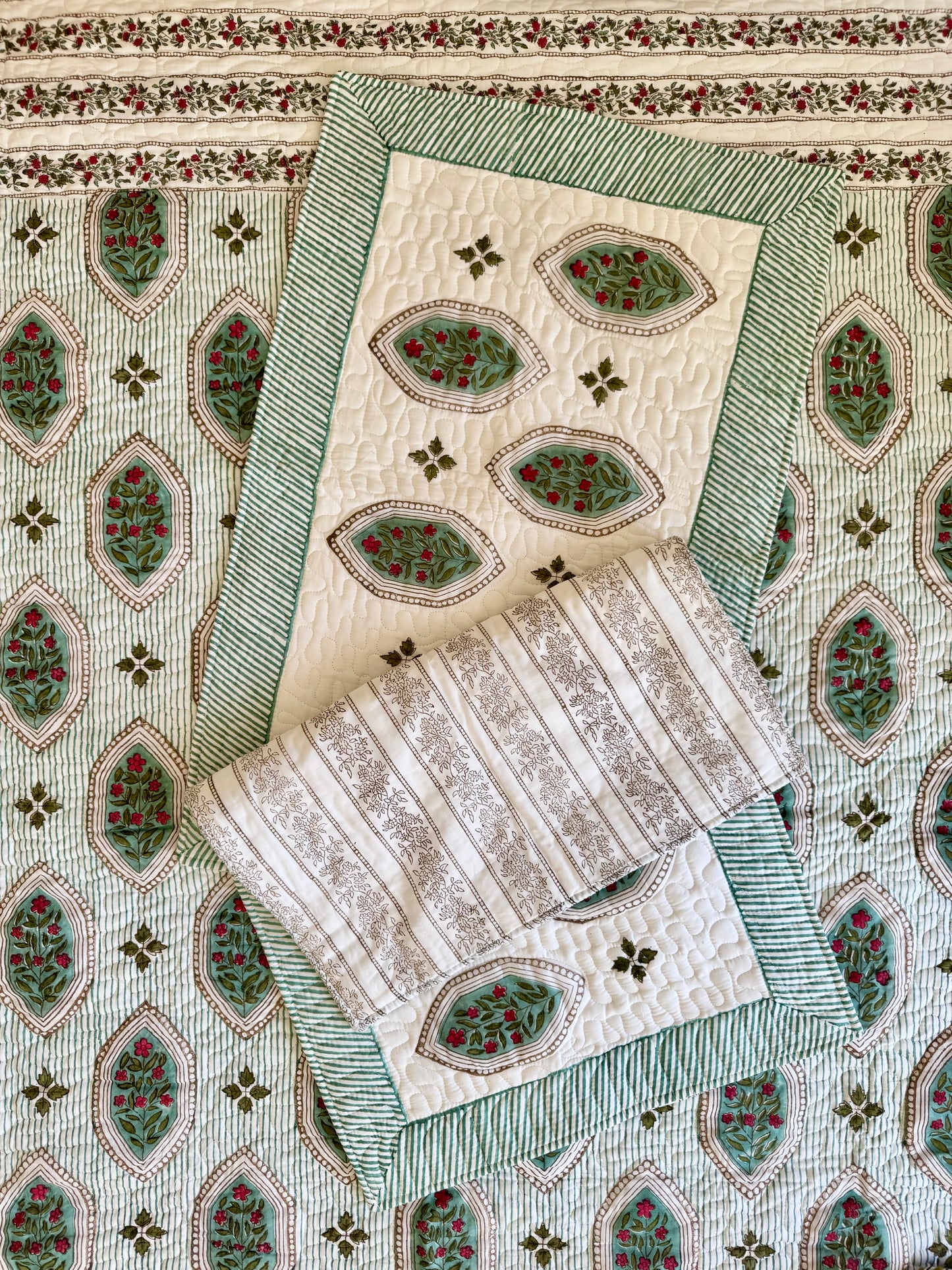 House of Mulmul - Blockprinted Cotton Bedcover. Reversible Bedspread. Bedroom with a floral-patterned quilt on a bed, framed mirror, pillowcases and curtains.