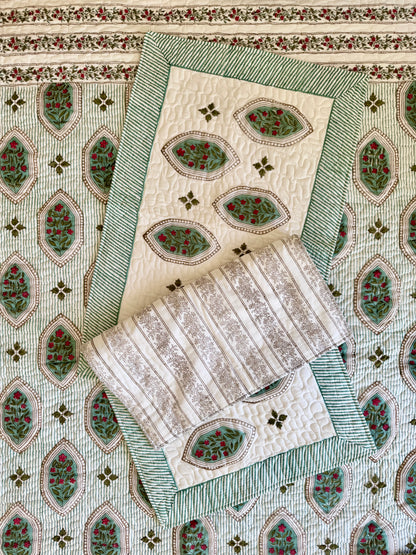 House of Mulmul - Blockprinted Cotton Bedcover. Reversible Bedspread. Bedroom with a floral-patterned quilt on a bed, framed mirror, pillowcases and curtains.