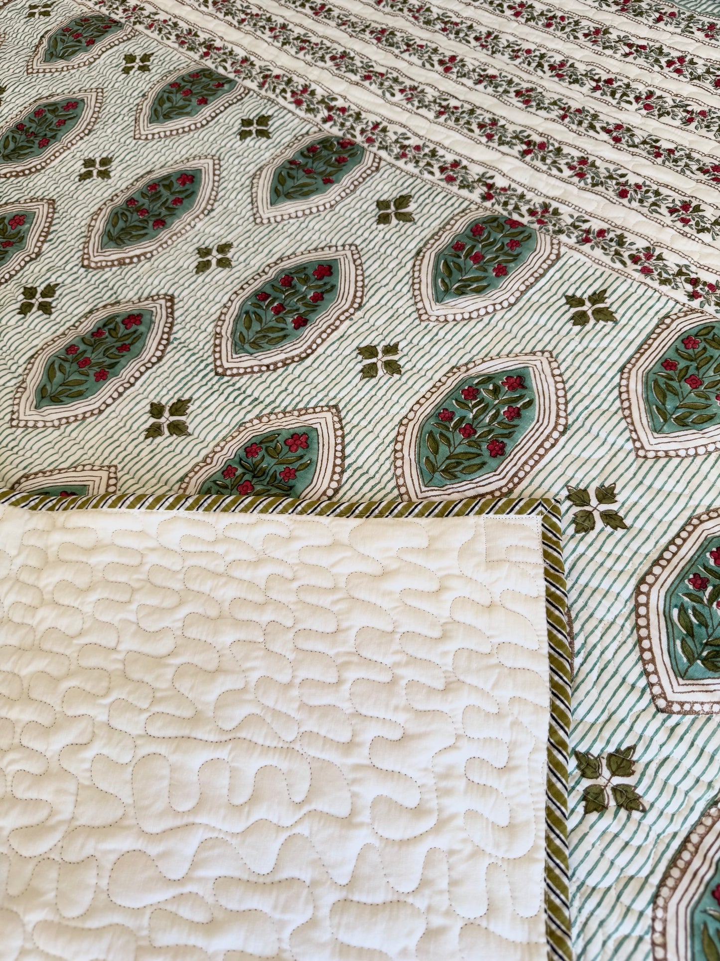 House of Mulmul - Blockprinted Cotton Bedcover. Reversible Bedspread. Bedroom with a floral-patterned quilt on a bed, framed mirror, pillowcases and curtains.