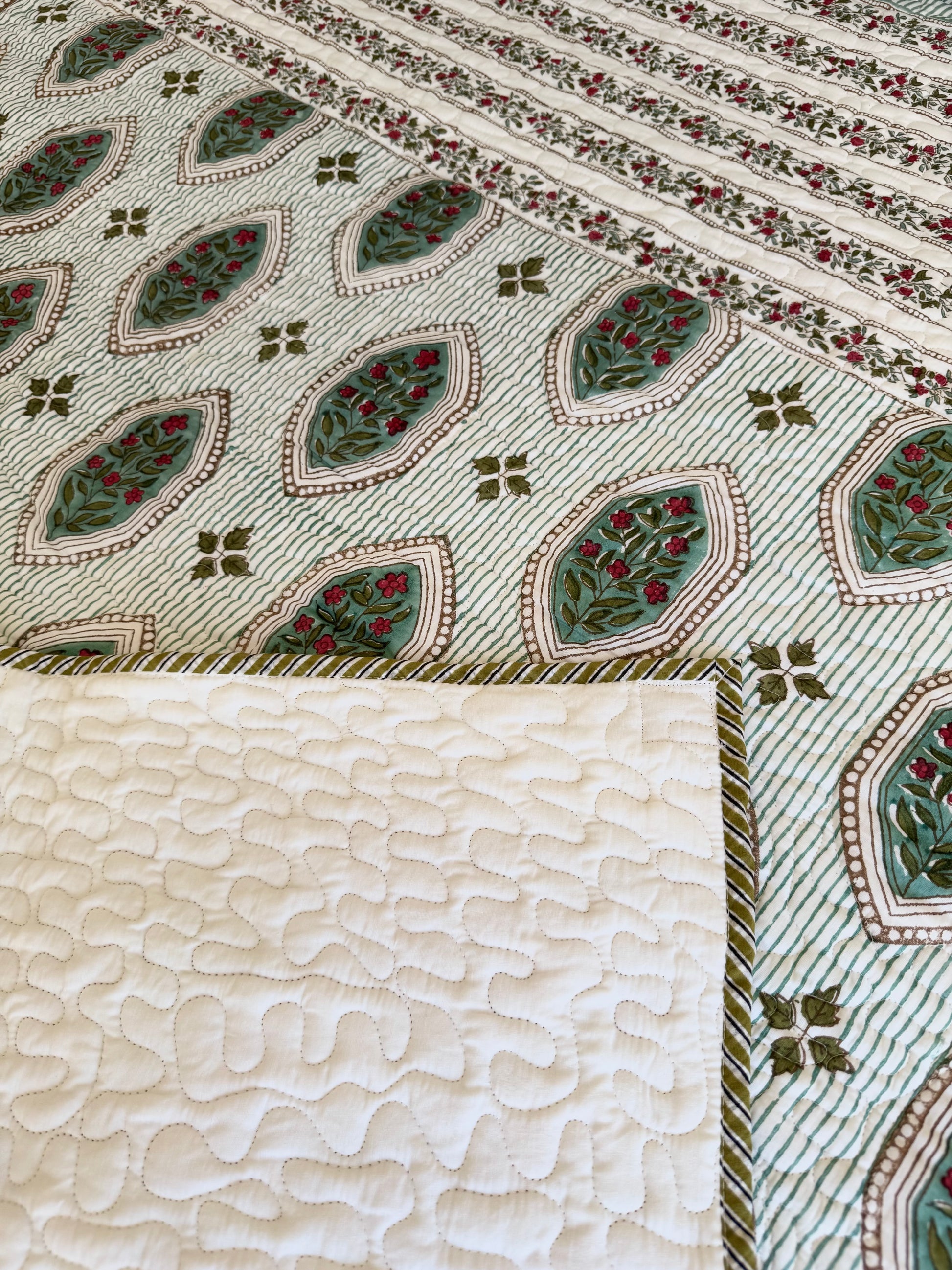 House of Mulmul - Blockprinted Cotton Bedcover. Reversible Bedspread. Bedroom with a floral-patterned quilt on a bed, framed mirror, pillowcases and curtains.