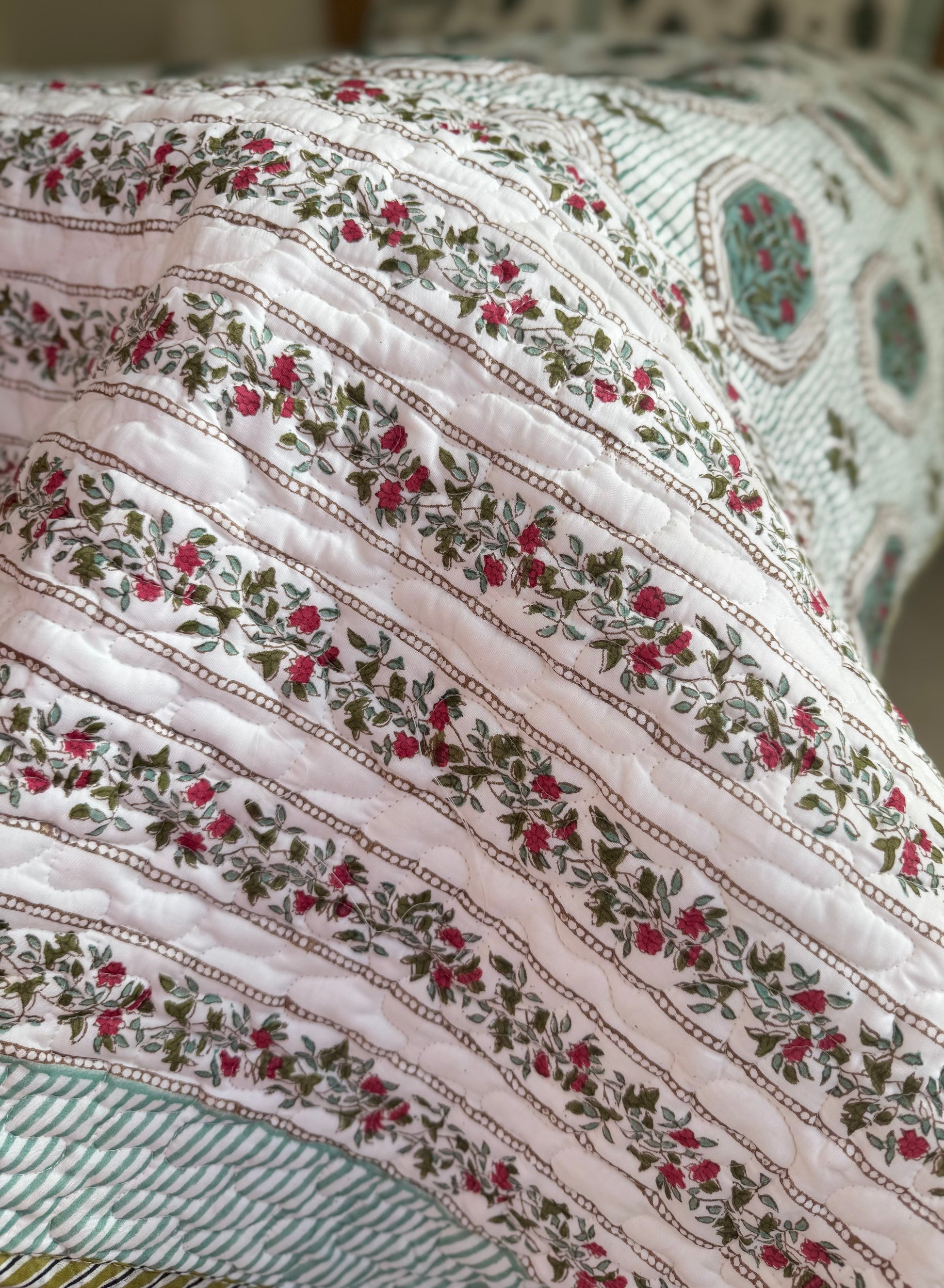 House of Mulmul - Blockprinted Cotton Bedcover. Reversible Bedspread. Close-up of a floral-patterned fabric with red flowers and green leaves on a white background.