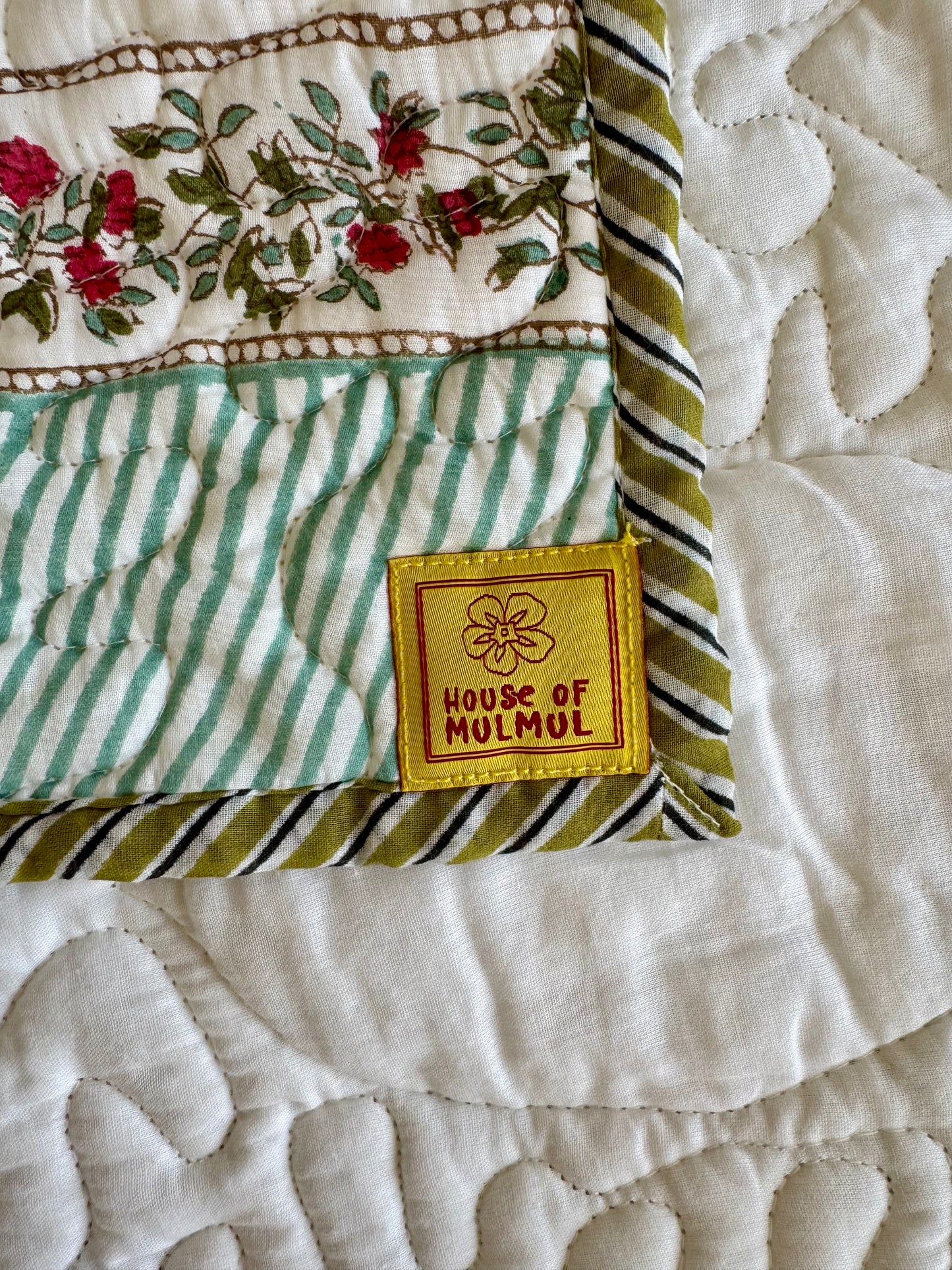 House of Mulmul - Blockprinted Cotton Bedcover. Reversible Bedspread. Bedroom with a floral-patterned quilt on a bed, framed mirror, pillowcases and curtains.