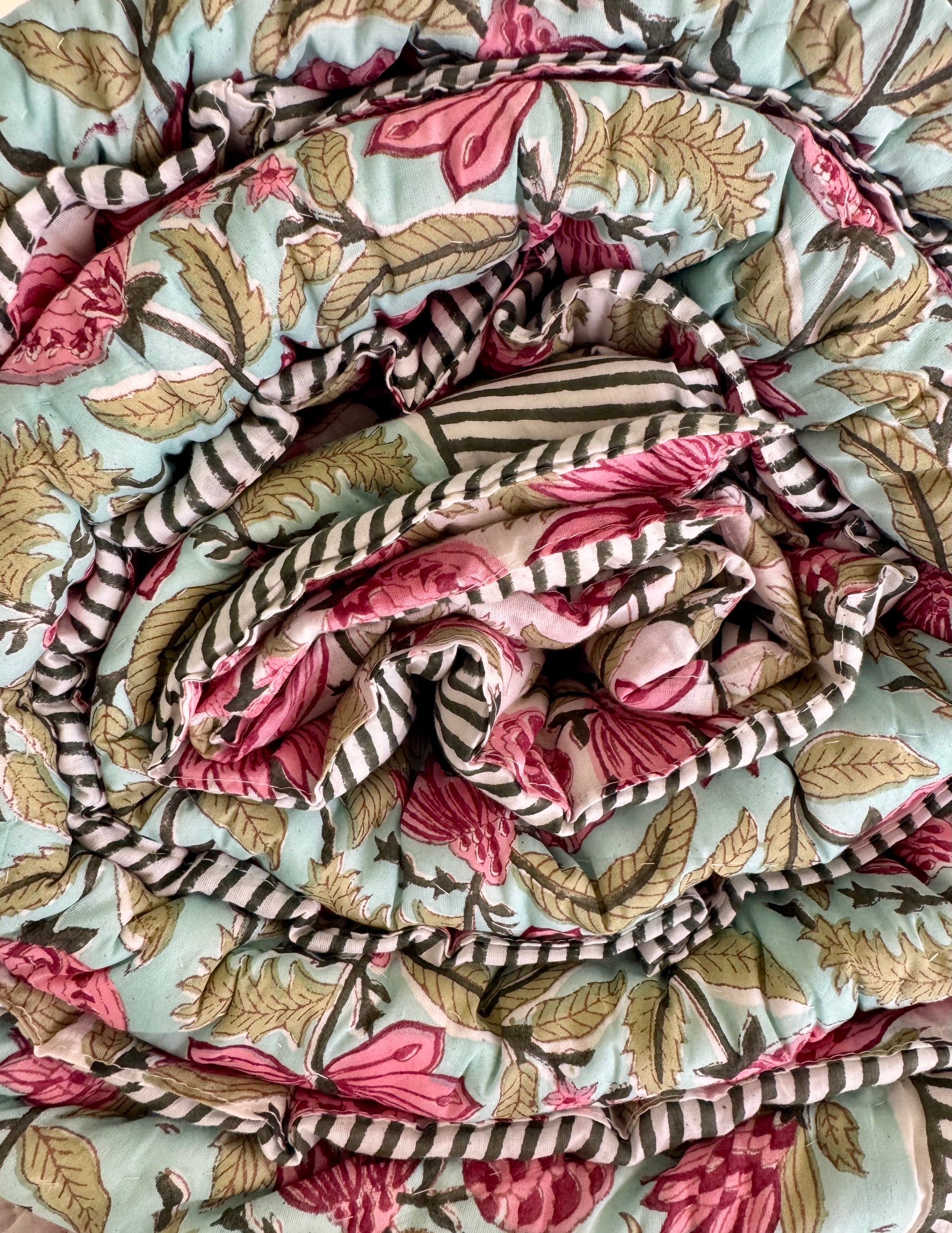 House of Mulmul - Blockprinted Cotton Quilt. Reversible Quilt. Rolled-up quilt with floral and striped patterns.