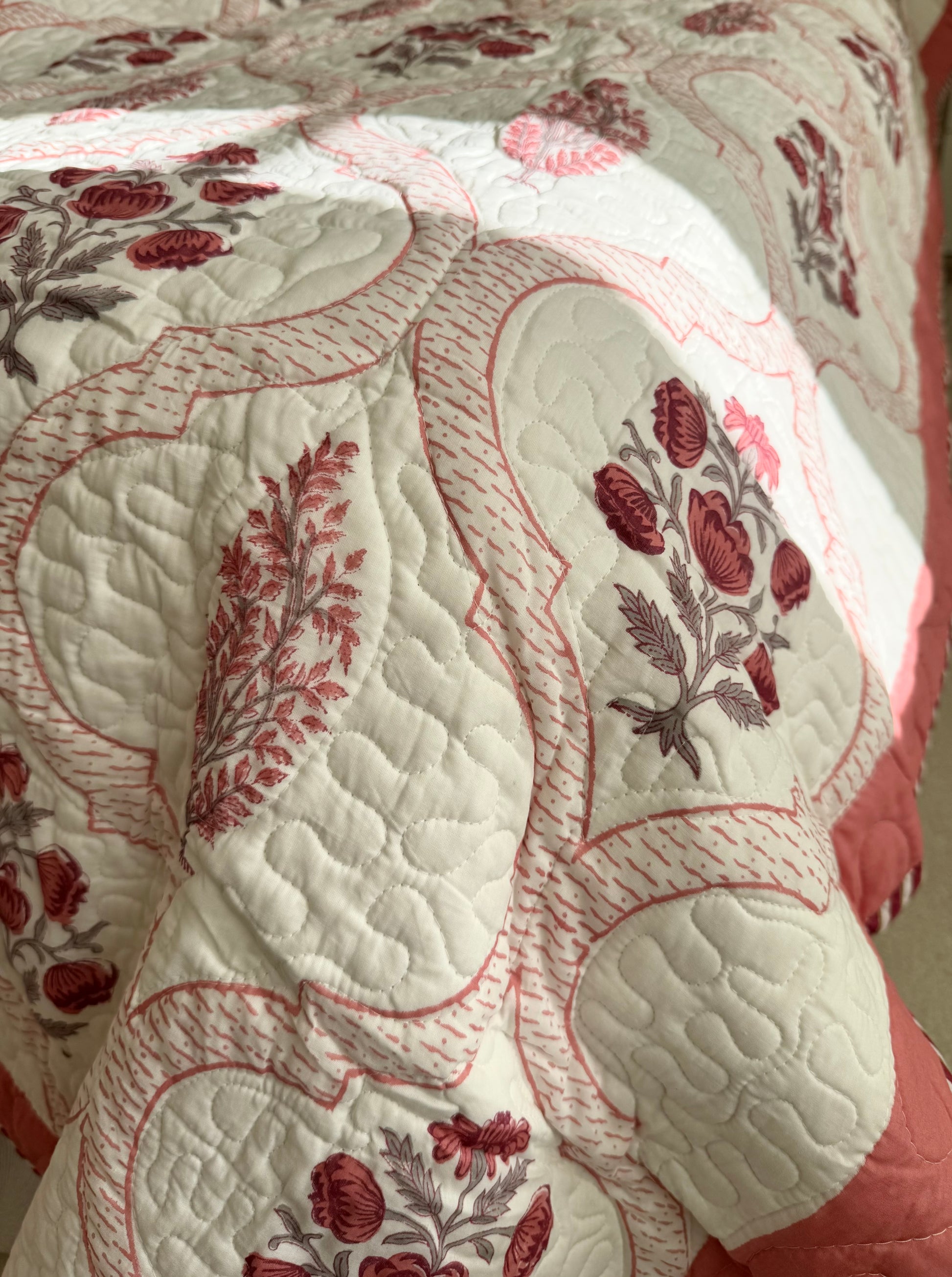 House of Mulmul - Blockprinted Cotton Bedcover Reversible Muslin. Close-up of a bedspread with floral patterns in red and beige.