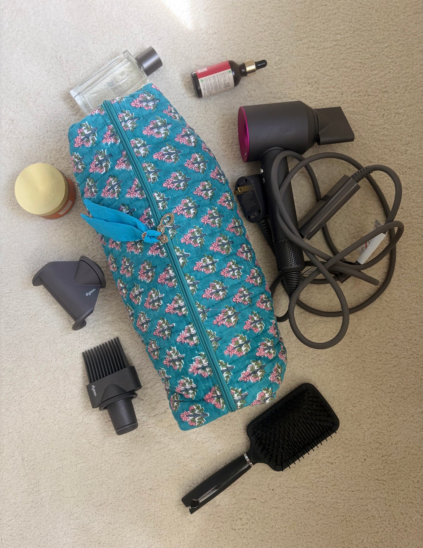 House of Mulmul - Blockprinted Cotton Hair Tool Bag. Floral-patterned Dyson hair dryer and straightener kit tool bag with hair dryer, attachments, and bottles on a beige surface
