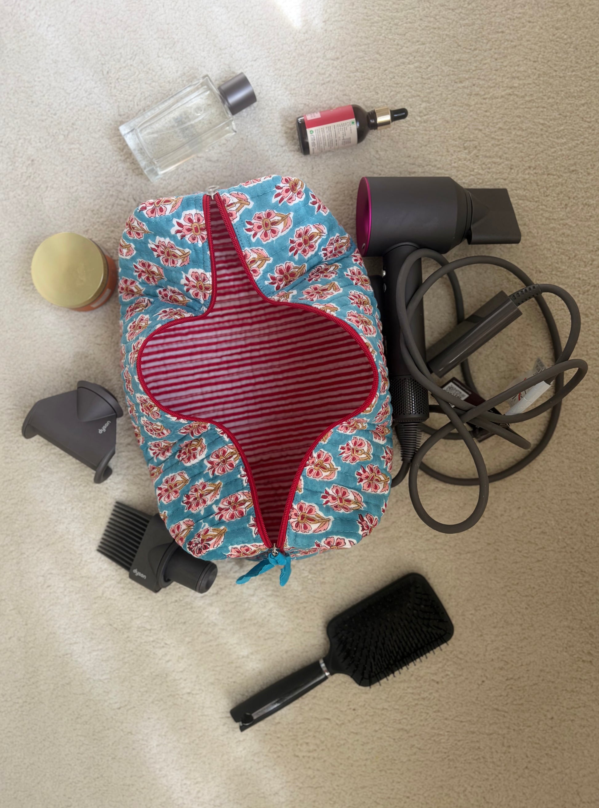 House of Mulmul - Blockprinted Cotton Hair Tool Bag. Floral-patterned hair dryer cover with Dyson hair dryer and straightener kit, brush, and bottles on a beige sure