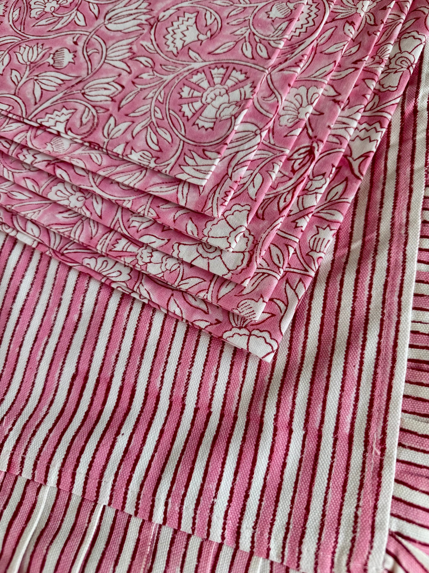 House of Mulmul - Blockprinted Cotton Placemats and Napkins. Close-up of a pink and white patterned placemats with floral napkins and striped designs.