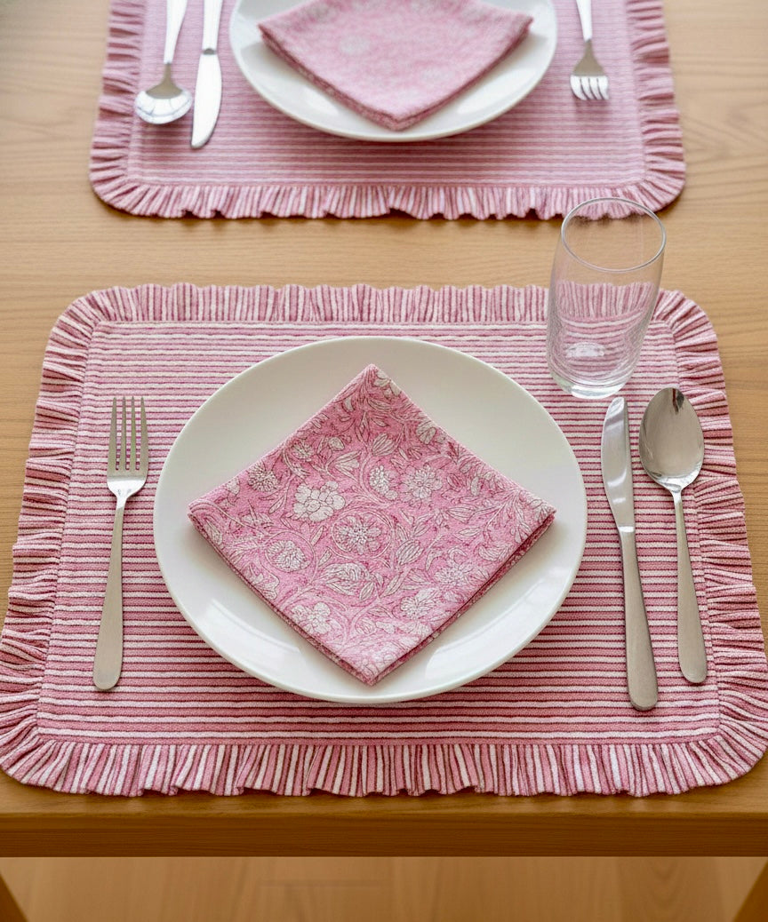 House of Mulmul - Blockprinted Cotton Placemats and Napkins. Table setting with pink striped placemats, white plates, silverware, and glasses on a wooden table.