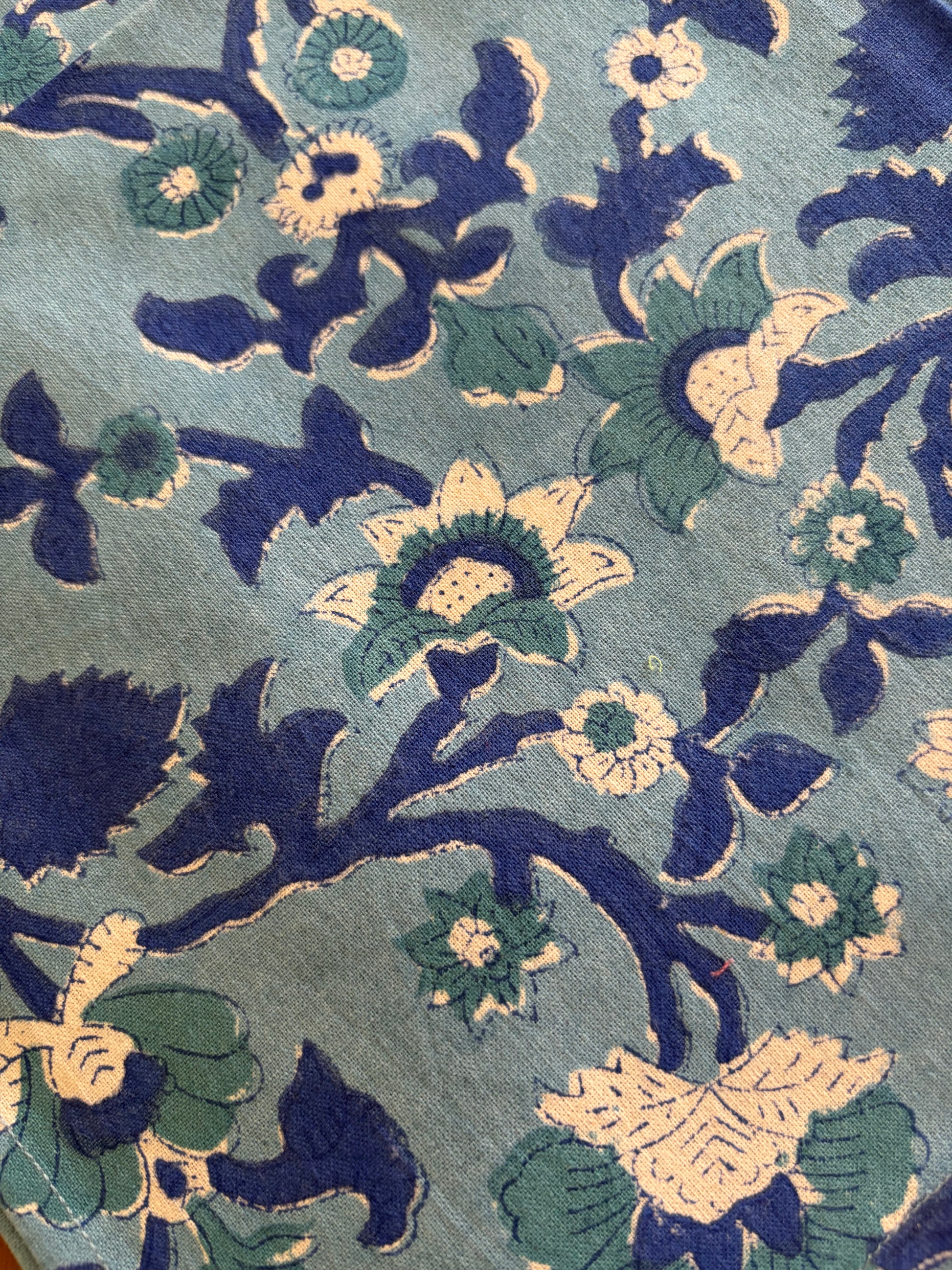 House of Mulmul - Blockprinted Cotton Table Napkins. Close-up of a floral pattern with blue, green, and beige colors on a textured fabric background.