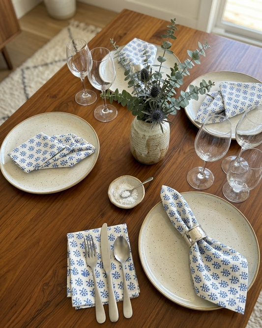 House of Mulmul - Blockprinted Cotton Table Napkins. Dining table set with plates, glasses, and floral napkins on a wooden table.