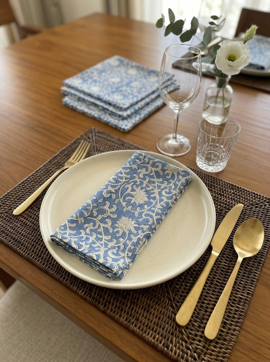 House of Mulmul - Blockprinted Cotton Table Napkins. Dining table setting with blue patterned napkins, white plate, gold cutlery, and a vase with flowers.