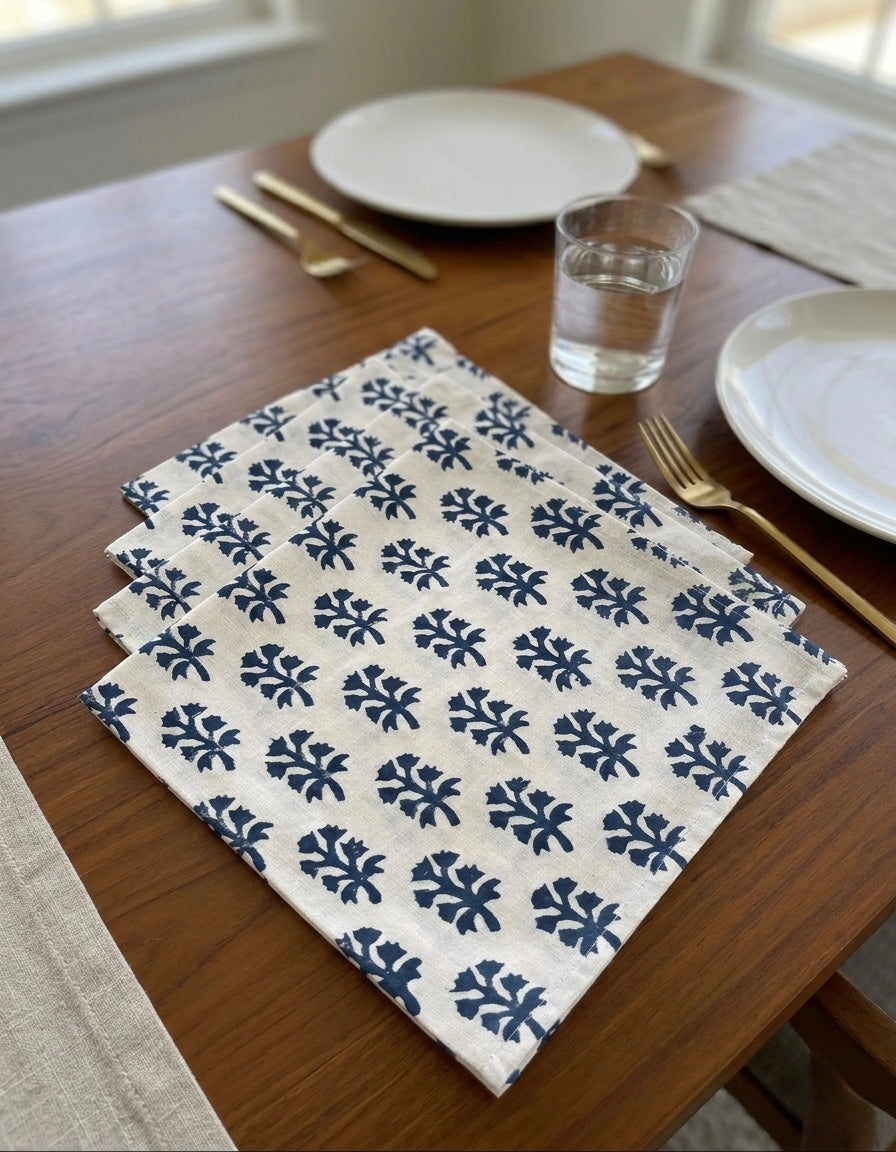 House of Mulmul - Blockprinted Cotton Table Napkins. Patterned white with blue design table napkin on a wooden table with plates, glasses, and cutlery.