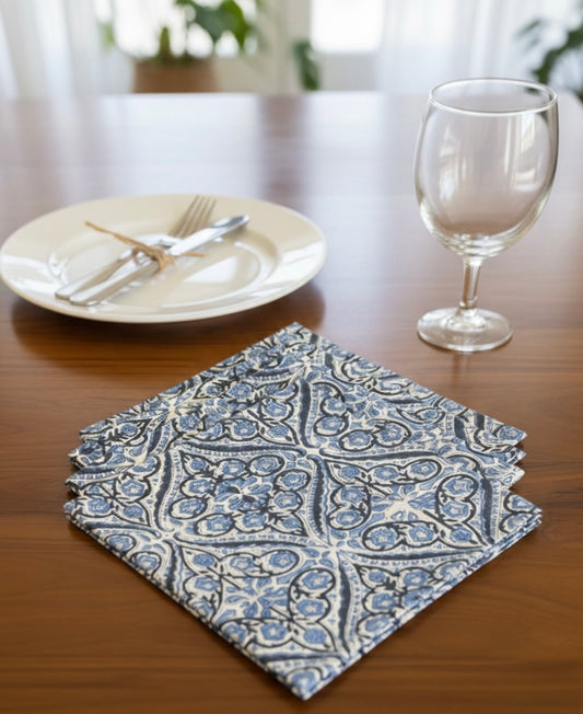 House of Mulmul - Blockprinted Cotton Table Napkins. Patterned blue white napkin on a table with a plate, fork, knife, and glass in the background.