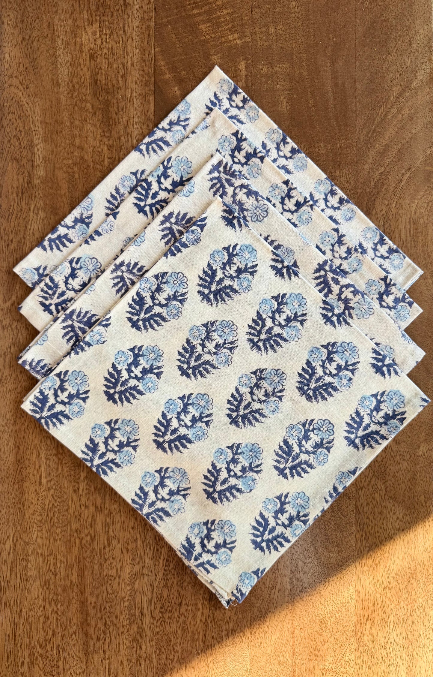 House of Mulmul - Blockprinted Cotton Napkins. Set of four folded fabric napkins with blue floral pattern on a wooden surface
