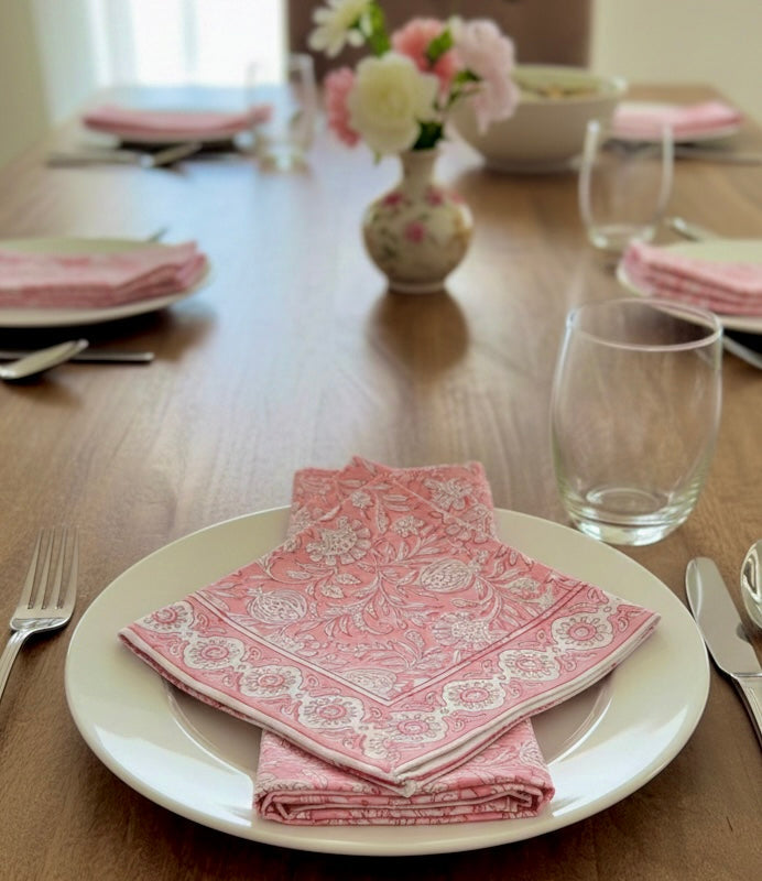 House of Mulmul - Blockprinted Cotton Napkins. Dining table set with pink patterned napkins on white plates, glasses, and cutlery.
