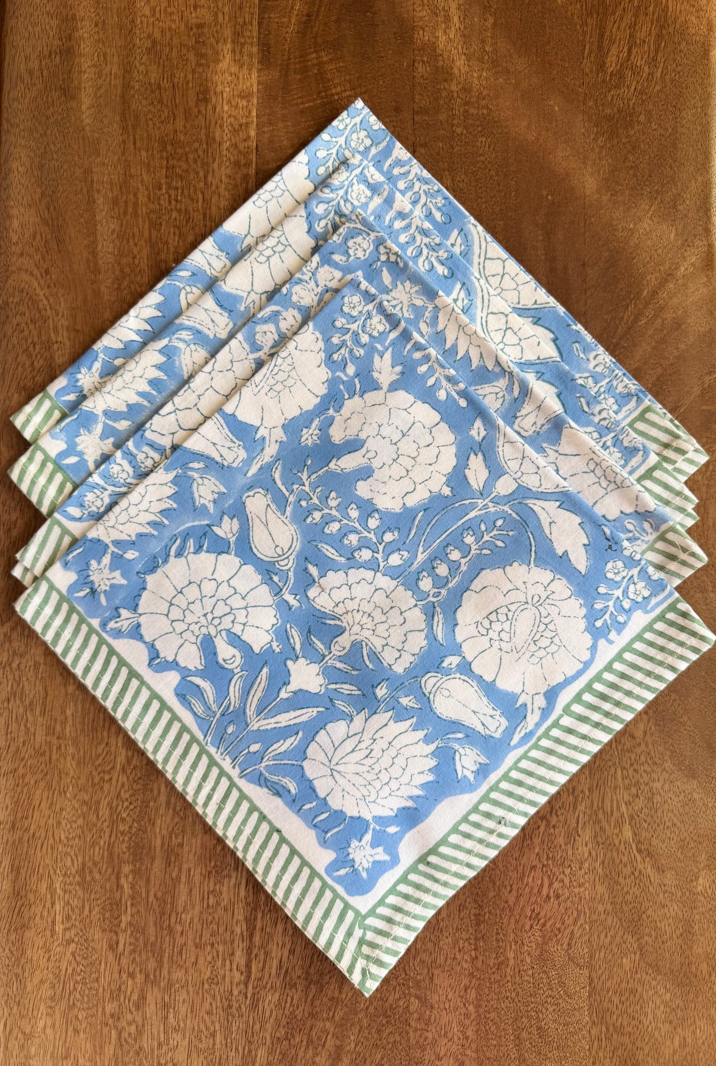 House of Mulmul - Blockprinted Cotton Napkins. Set of floral-patterned napkins with green stripes on a wooden surface