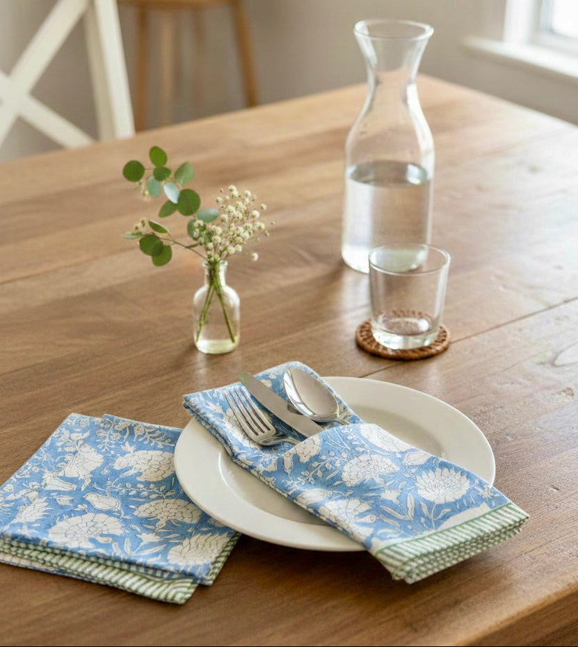 House of Mulmul - Blockprinted Cotton Napkins. Dining table setting with floral-patterned napkins, cutlery, and a carafe of water.