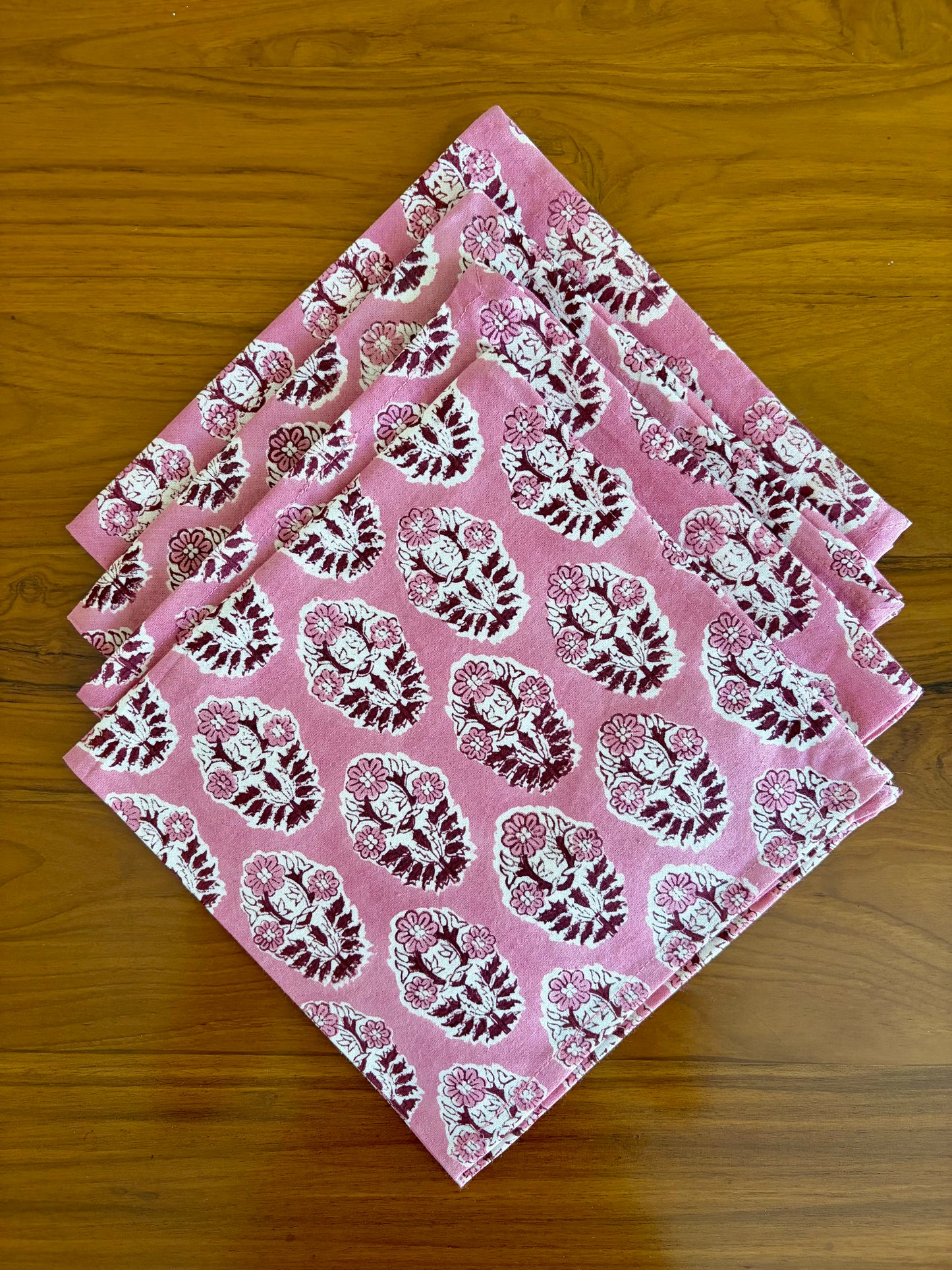 House of Mulmul - Blockprinted Cotton Table Napkins. Set of pink napkins with white floral patterns on a wooden surface