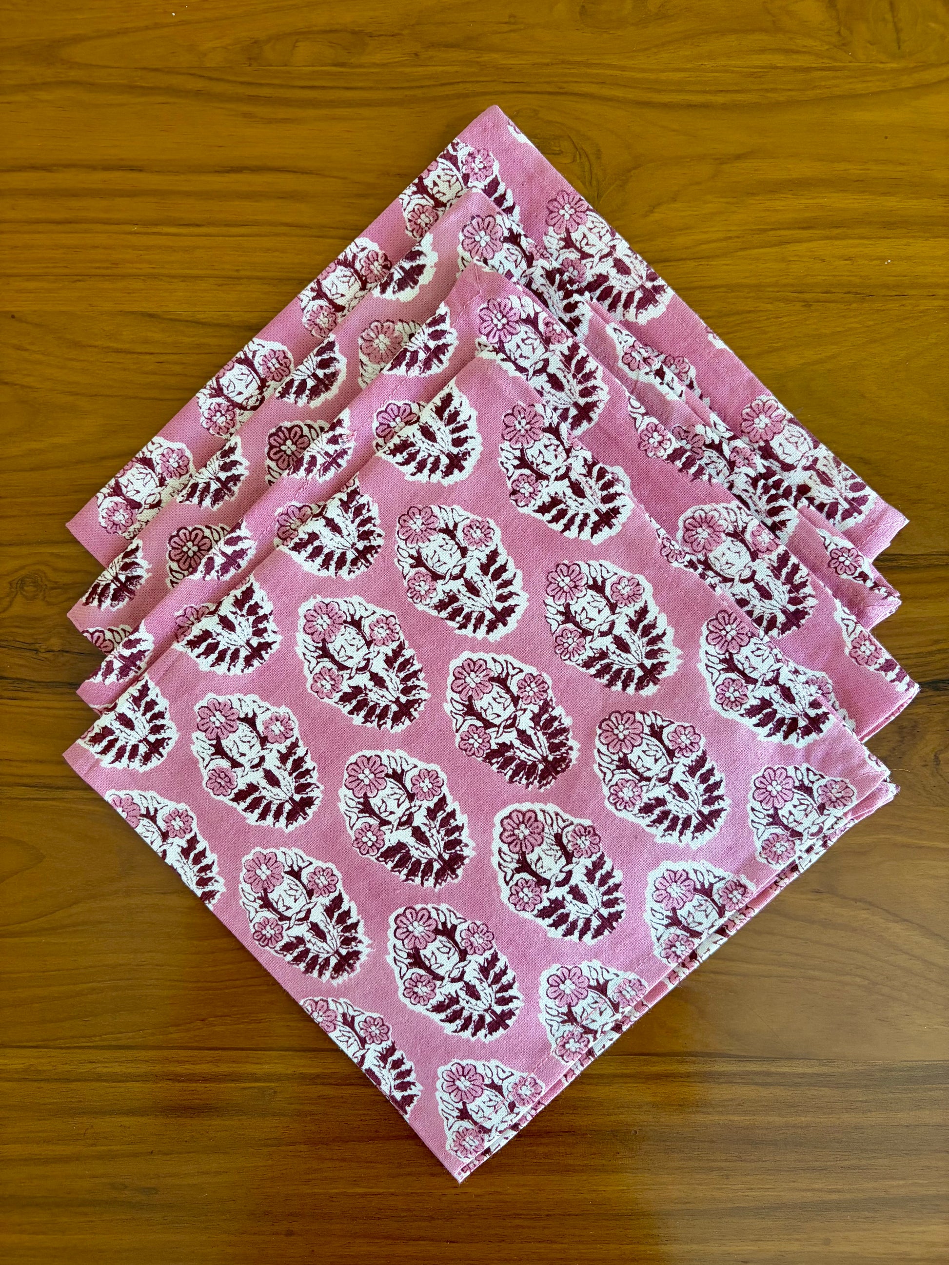 House of Mulmul - Blockprinted Cotton Table Napkins. Set of pink napkins with white floral patterns on a wooden surface