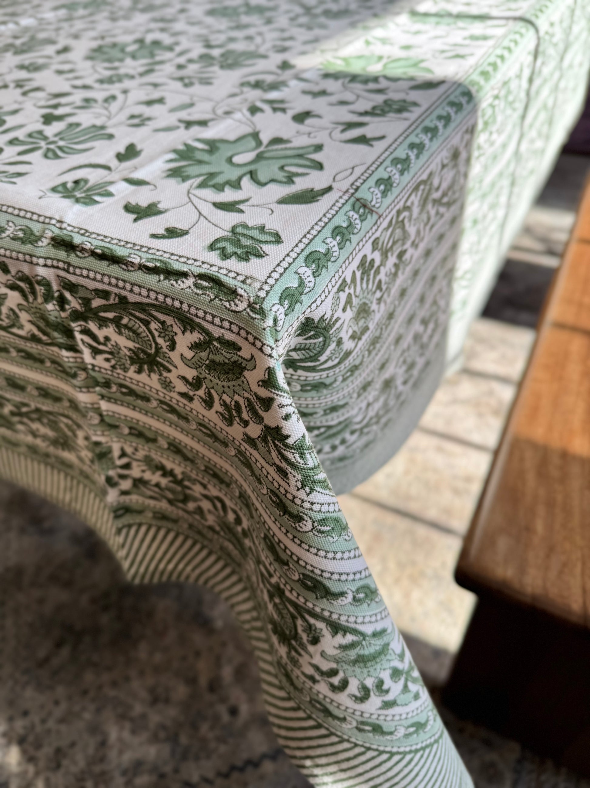 House of Mulmul - Blockprinted Cotton Table Cloth. Cotton tablecloth with green and white colors and flowers. Close-up of a patterned tablecloth on a table with a blurred background