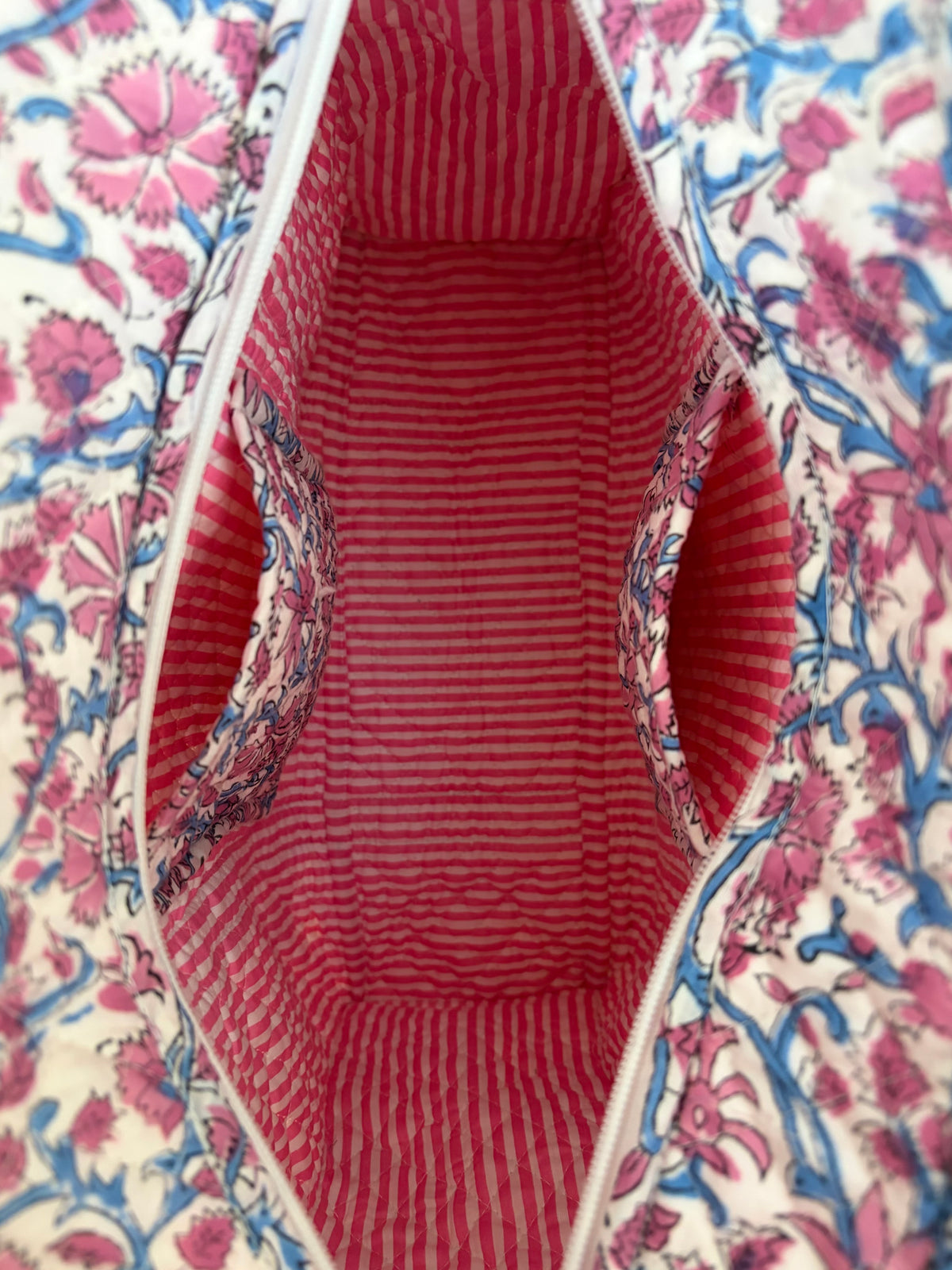 House of Mulmul - Blockprinted Cotton Tote Bag, Travel Bag. Close-up of a fabric bag's open interior, showing a red and white striped lining with patterned fabric pockets, surrounded by a pink, blue, and white floral print exterior.