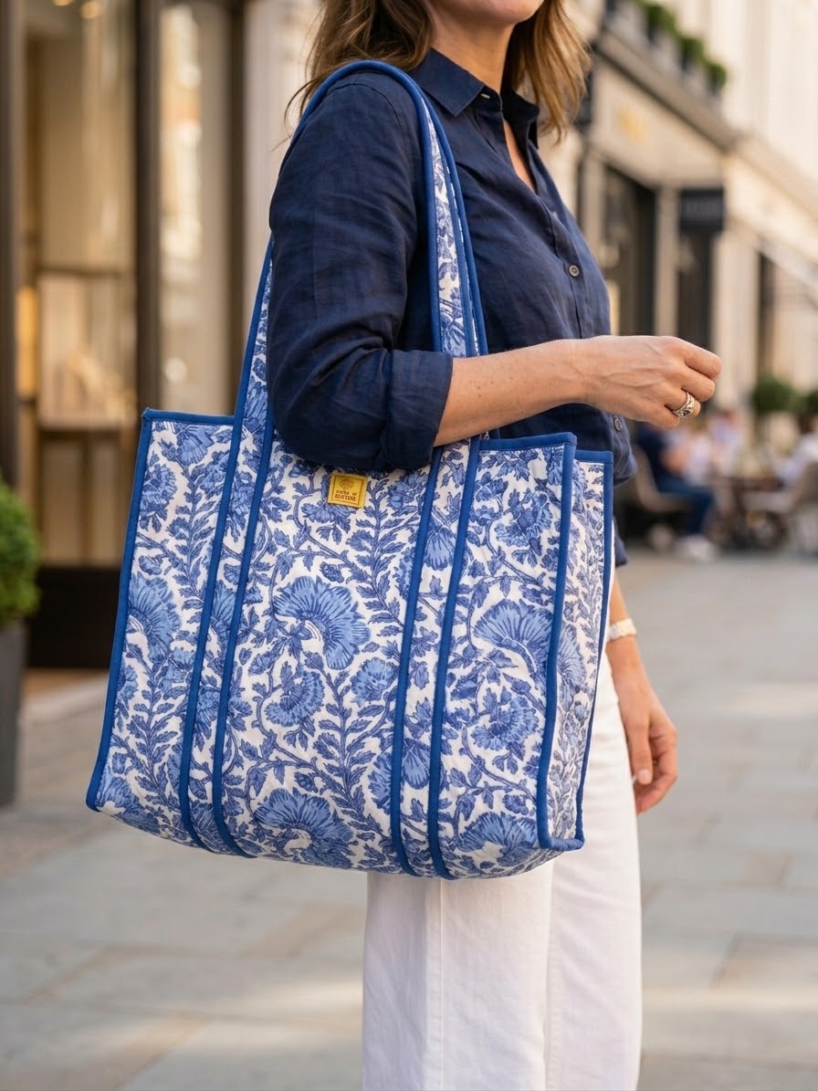 House of Mulmul - Blockprinted Cotton Tote Bag, Travel Bag. A woman wearing a navy shirt and white trousers carries a large blue and white floral patterned tote bag on her shoulder in an outdoor urban setting.