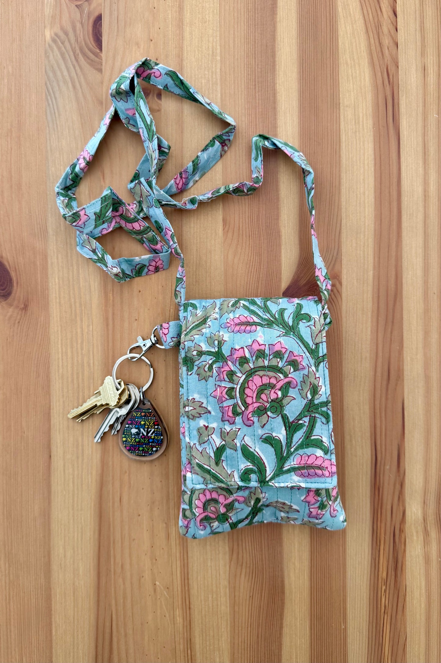 House of Mulmul - Blockprinted Crossbody Mobile Sling Bag. Floral patterned keychain with a small pouch on a wooden surface